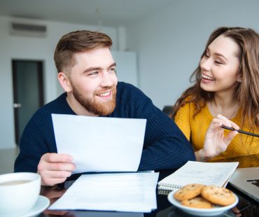 A young couple laughs at a table with small business HSA papers.