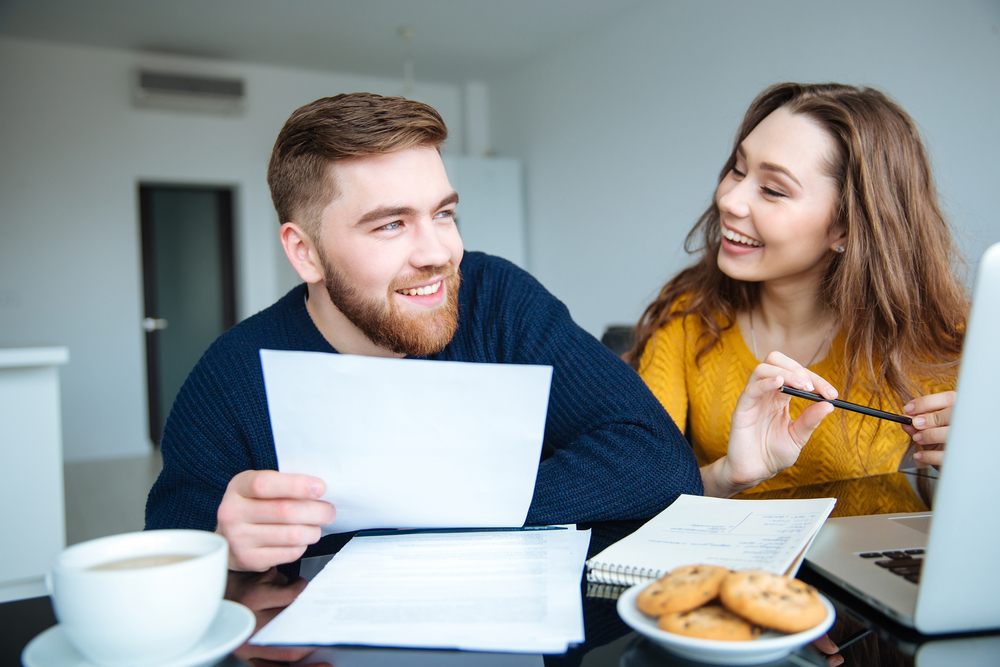 A young couple laughs at a table with small business HSA papers.